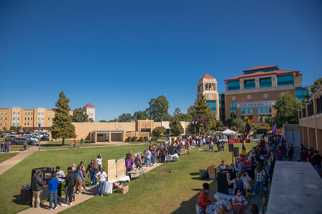 People mingle at booths and tables in the quad on ɫAV's campus. A banner hanging from the library in the background reads "The Best is on the Bayou."